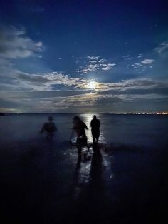 three people are walking on the beach at night