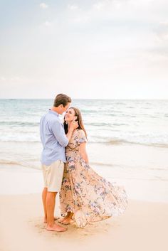 an engaged couple standing on the beach in front of the ocean