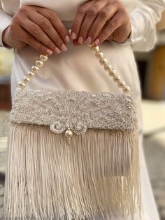 "Luxurious fringe vintage-looking wedding clutch is handmade and decorated with Italian lace. seed beads, pearl beads, and cute dangling fringe. The glamorous small bridal handbag on the beaded strap (pearl imitation) will be a great addition to your amazing bohemian look on the Special Day! The tiny ivory elegant evening bag has a fold-over lace cover and closes with a magnetic clasp. It will be a great accessory addition for the bride in a bohemian style. The fancy classic women purse will als Luxury Party Clutch With Fold Over Clasp, Luxury Evening Clutch With Fringe, Luxury Fringe Clutch For Women, Luxury Hand-embellished Glamorous Evening Bag, Luxury Evening Pouch Flap Bag, Luxury Handheld Shoulder Bag For Wedding, Luxury Shoulder Bag For Reception, Luxury Glamorous Bag For Reception, Classic Luxury Flap Bag For Evening