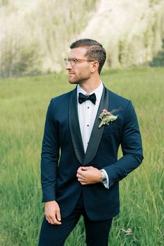 a man in a tuxedo poses for the camera with his hand on his hip