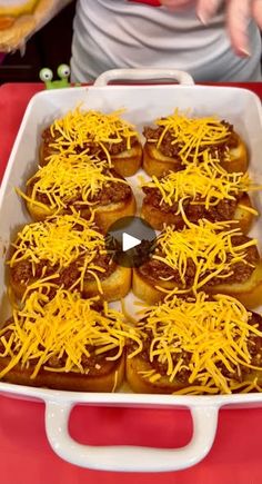 a white dish filled with chili cheese covered hot dogs on top of a red table