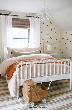 a white bed sitting under a window next to a basket on top of a rug