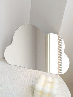 a white cloud shaped mirror sitting on top of a bed next to a wall mounted light