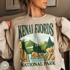 "Show off your love of nature and our nation's beautiful parks in our Kenai Fjords National Park Sweatshirt! This sweatshirt is all about embracing the great outdoors, featuring a custom design that showcases the  beauty of the Alaskan Wilderness and the stunning Kenai Fjords! Remember that once in a lifetime Alaskan Cruise or epic Alaskan adventure with this one of kind crewneck! The Gildan 18000 cotton fabric has that comfy, lived-in feel, that's like a hug every time you put it on! Now you can take a bit of Kenai with you wherever you wander! Grab one while you can, and hit the trail! * Product Highlights * Ideal for any situation, this Gildan 18000 heavy blend crewneck sweatshirt is pure comfort. Made from an extremely soft 50/50 polyester and cotton blend, this combination helps keep National Park Sweatshirt, Sweat Vintage, Kenai Fjords National Park, Capitol Reef, Badlands National Park, Gifts For Campers, Bryce Canyon National Park, Outdoor Shirt, Grand Canyon National Park