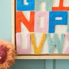 a teddy bear sitting in front of a wooden letter wall hanging on a blue wall