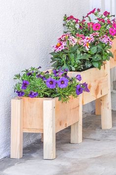 two wooden planters with purple and white flowers in them sitting on the side of a building