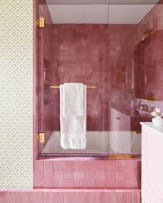 a bathroom with pink tiles and white towels hanging on the shower door, next to a sink