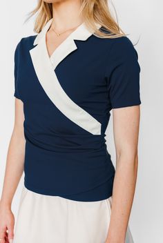 Tee up your style with the Parks Top by G&T Sport. This figure-flattering polo features a wrap-over label, ruched waist, and V-neckline for a polished, yet effortless look on the green or off. The classic polo silhouette and sporty aesthetic make it a versatile choice for the golf course, driving range, or casual weekend. Classic Navy V-neck Top, Navy Stretch V-neck Top, Elegant Fitted Wrap Top With Foldover Design, Navy Chic Fitted Tops, Chic Navy Fitted Tops, Chic Navy V-neck Top, White Fitted V-neck Wrap Top, Fitted V-neck Wrap Top, Navy Fitted Tops For Workwear