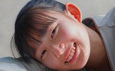 a young boy smiling and wearing a gray shirt with his head tilted to the side