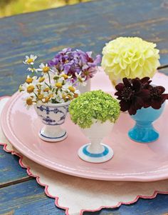 three vases with flowers are sitting on a pink plate