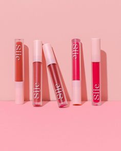 five lip glosses lined up on a pink surface