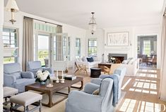 a living room filled with white furniture and lots of windows covered in curtains on either side of the couches