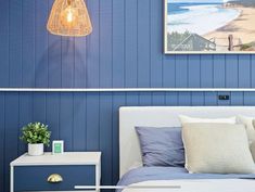 a bedroom with blue walls and white bedding has a lamp on the nightstand next to it