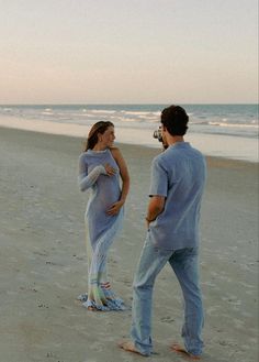 a man and woman standing on top of a sandy beach next to the ocean,