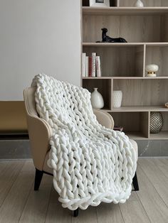 a white knitted blanket sitting on top of a chair in front of a book shelf