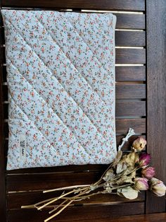 a quilted pillow sitting on top of a wooden bench next to dried flowers