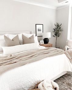 a bed with white linens and pillows in a bedroom next to a lamp on a table