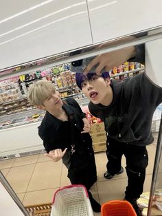 two young men standing next to each other in front of a store display case and looking into the mirror