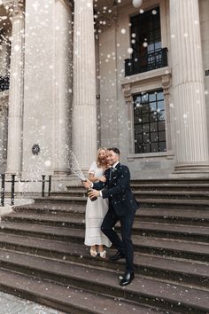 a newly married couple standing on steps in front of a building with snow falling from the sky