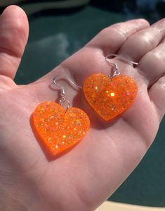 "Each pair of resin earrings are handmade to order, therefore no two pairs are identical! However, I try to get as close as possible :) Made with nickel free & hypoallergenic sterling silver plated fish hooks. Heart width is approximately 1.25\", and is made with epoxy resin and neon orange holographic and iridescent glitter! 🧡 Ultraviolet / blacklight reactive, sparkly dangly heart earrings! Perfect for Halloween, concerts, raves, parties, etc.  Thanks for visiting my shop! ✨" Cute Orange Jewelry For Party, Cute Orange Party Jewelry, Heart-shaped Orange Jewelry For Gift, Orange Heart-shaped Jewelry Gift, Handmade Orange Heart Jewelry, Handmade Heart-shaped Orange Jewelry, Handmade Orange Heart-shaped Jewelry, Orange Heart Beads Jewelry For Gift, Orange Jewelry With Heart Beads For Gifts