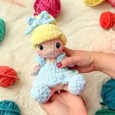 a hand holding a small crocheted doll in front of balls of yarn