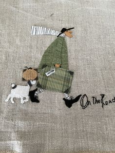 a woman walking with two dogs on the ground next to a piece of fabric that has been embroidered onto it