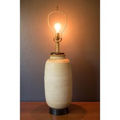 a white vase with a light on top of it sitting on a table next to a wall