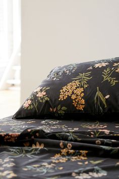 a bed covered in black floral sheets and pillows