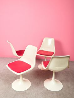 three chairs and a table in front of a pink wall