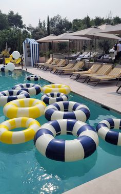 several inflatable floats floating on top of a swimming pool next to lounge chairs and umbrellas