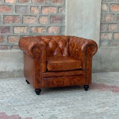 a brown leather chair sitting on top of a brick floor next to a stone wall