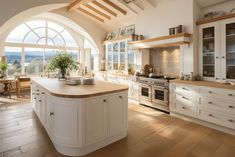 a large kitchen with an arched window and wooden flooring, along with white cabinets