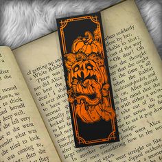 an orange and black bookmark sitting on top of an open book with pumpkins