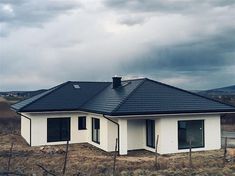 a white house with a black roof in the middle of an open field under a cloudy sky