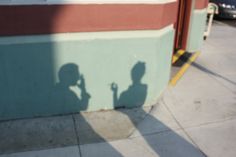 the shadow of a person holding a cell phone is cast on a building wall next to a parking lot