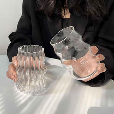 a woman sitting at a table holding a clear glass vase with her hands on it