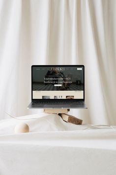 an open laptop computer sitting on top of a wooden table next to a white curtain