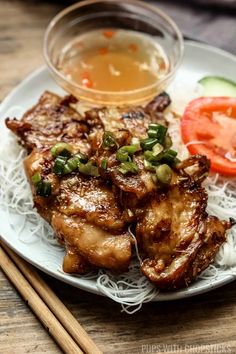 a white plate topped with meat and veggies next to chopsticks on top of a wooden table