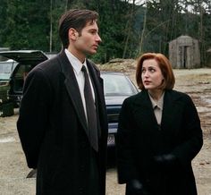 a man and woman standing next to each other in front of a car on a dirt road