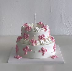 a white cake with pink icing and a single candle on top is sitting on a table