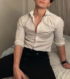 a man sitting on top of a bed wearing black pants and a white button up shirt