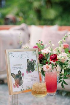 a table topped with drinks next to a vase filled with flowers and an animal sign