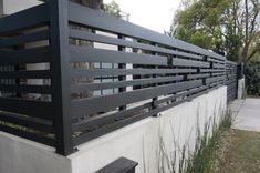 a black metal fence on the side of a white wall next to a tree and grass