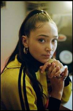 a young woman with long hair and piercings on her ear, wearing a yellow jacket