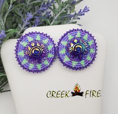 These are authentic Native American earrings, hand crafted by a member of the Muskogee Creek Tribe. Used in the handmade process are seed beads, acrylic cabochons and faux leather backing. The bead colors included in this pair are:  green and purple seed beads. They measure 1 1/2 inches wide and 1 1/2 inches long. They have stainless steel hypo-allergenic lever back ear post for pierced ears.