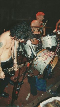 a man with long hair playing drums in front of two other men on the stage