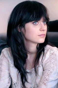 a woman with long black hair and blue eyes sitting on a couch looking off to the side