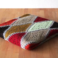 a multicolored crocheted blanket sitting on top of a wooden floor next to a cup