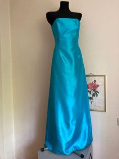 ♥ Vintage strapless maxi formal dress/gown - effortless luxury and elegance. ♥ The bust fitted with 4 bones, form-fitting.  ♥ Dramatic back pleat-short train. ♥ Color: vibrant turquois.  ♥ Polyester fabric.  ♥ Not lined, with zipper on the back. ♥ Good vintage condition, no major imperfections, only some minor signs of wear. I noticed some barely noticeable fraying on some seams, see last photo. ♥ Brand: Australian designer Ruth Tarvydas, who was famous for her exquisite high-end party dresses and ball gowns, which attracted tons of celebrities.  This find is very special to me, as a Lithuanian, and I loved doing some research: Ruth Tarvydas was born to Lithuanian parents, Martynas and Ursula Tarvydas. Ruth's first label, 'Ruta' (or Rūta, her original Lithuanian first name), was establishe Floor-length Turquoise Gown For Party, Turquoise Floor-length Gown For Party, Turquoise Evening Dress For Party, Elegant Turquoise Evening Dress For Prom, Elegant Turquoise Evening Gown, Elegant Turquoise Dress With Fitted Bodice, Green Strapless Gown For Formal Occasions, Blue Floor-length Strapless Dress For Prom, Formal Green Strapless Gown