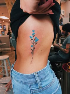 a woman's lower back tattoo with blue flowers on her left side ribcage